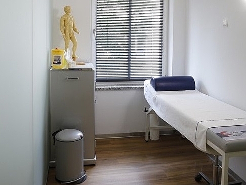 Ein Untersuchungszimmer mit einer Liege und einem Schrank.